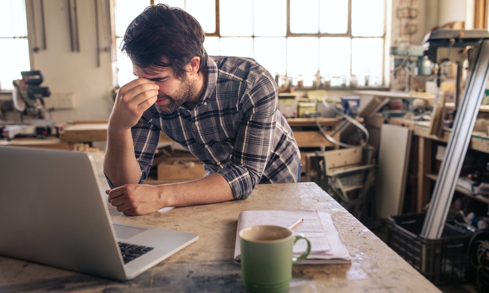 Young,Woodworker,Looking,Tired,While,Leaning,At,A,Workbench,In